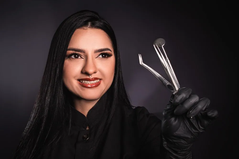 A dentist holding instruments against a dark background